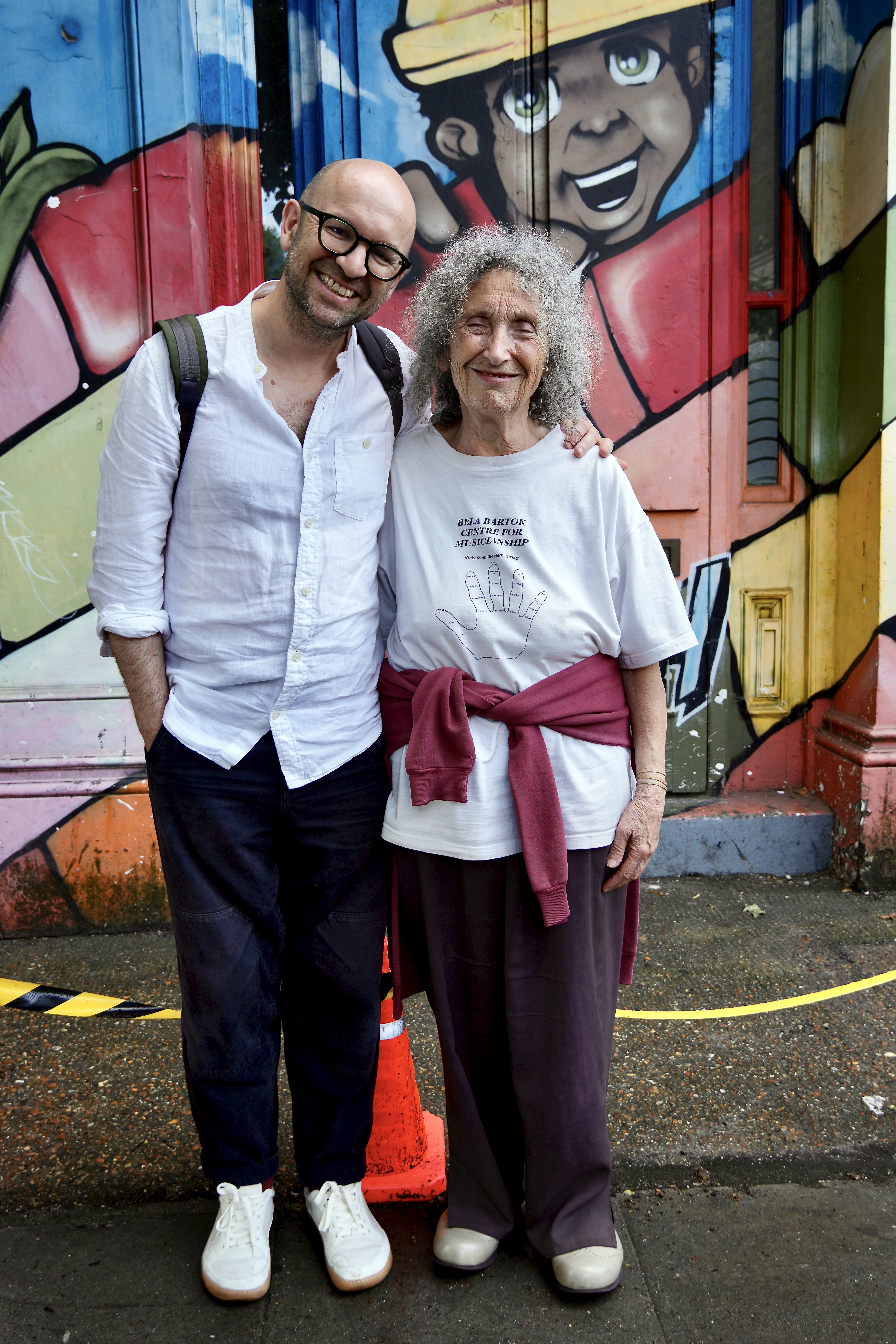 A photograph of Thomas Guthrie and Agnes Korie smiling, in front of a wall full of graffiti