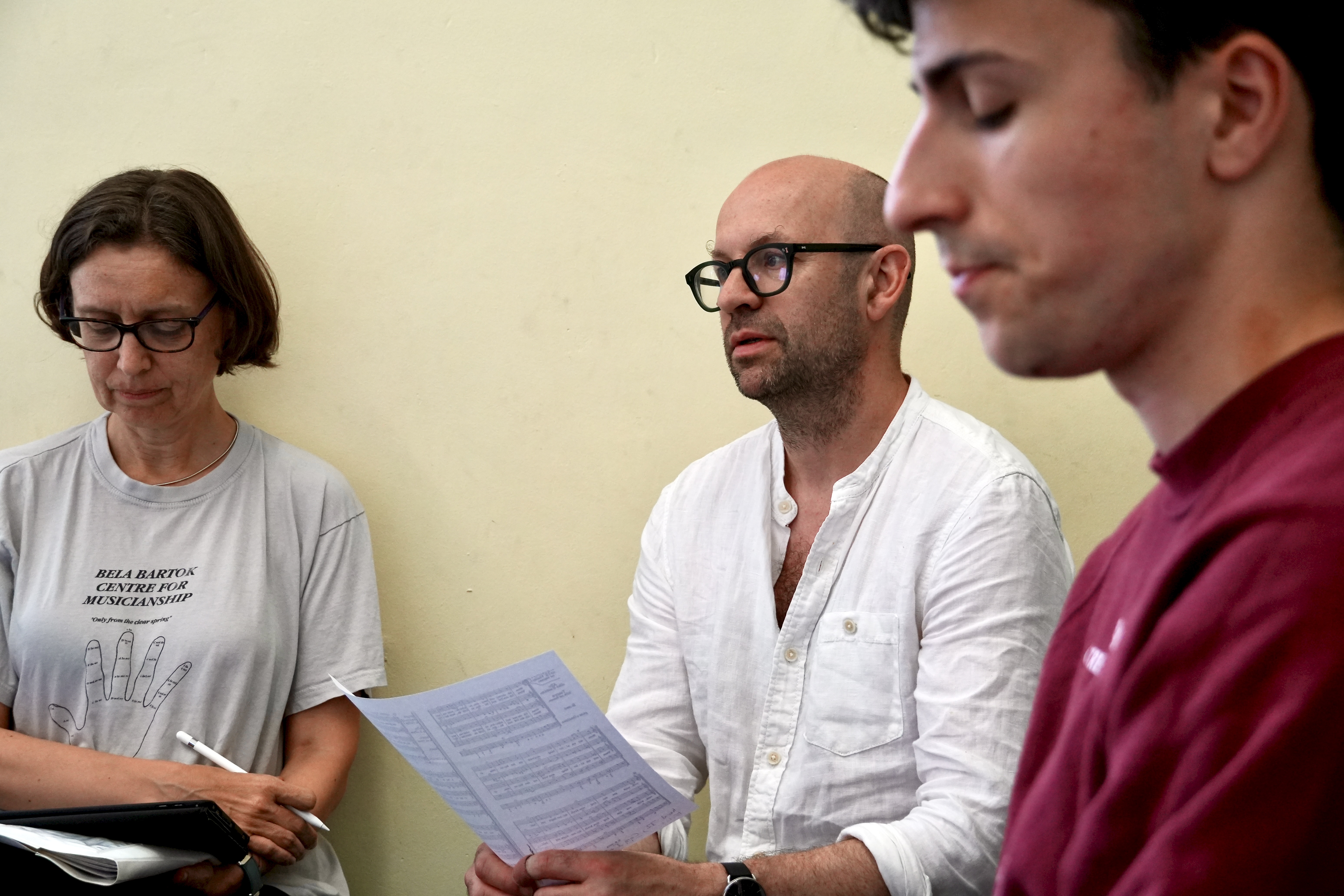 A photograph of three adults, one female and two male, looking at sheet music