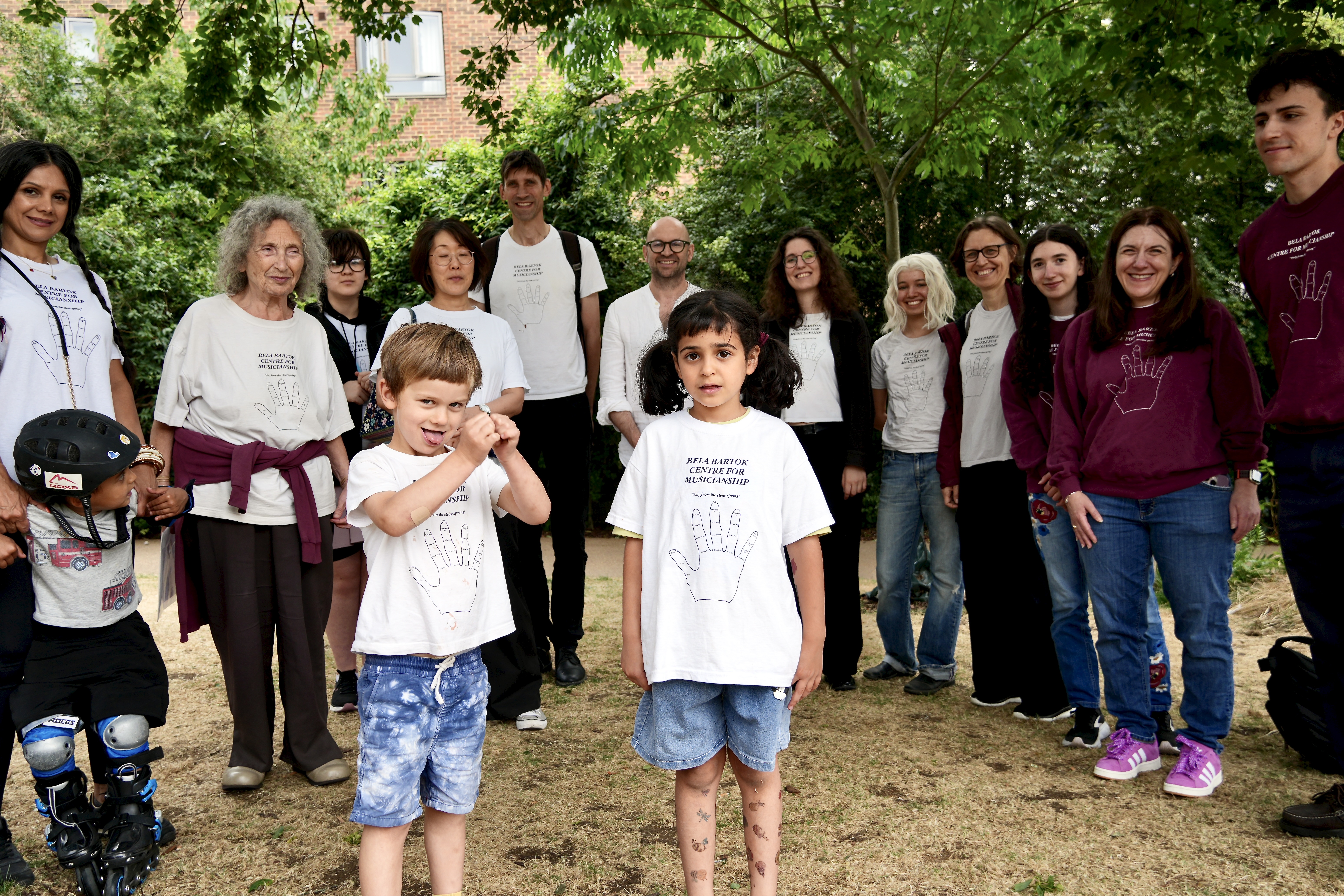 Picture of a group of people, mostly adults, with two young children in front. One looks serious, one pulls a funny face